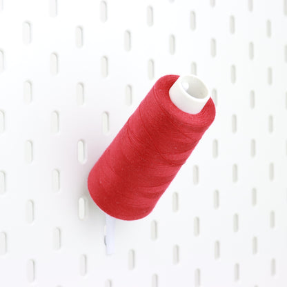 Röd sytrådsrulle på en vit hållare monterat på Ikea Skådis tavlan